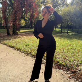 Czarny kombinezon Virelle na modelce — cała sylwetka, ujęcie z uniesioną ręką